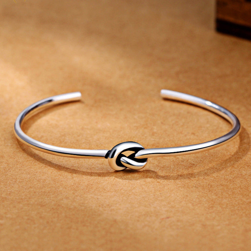 Elegant open-ended Luxury Metal Bracelet with a sleek knot design on a warm brown background