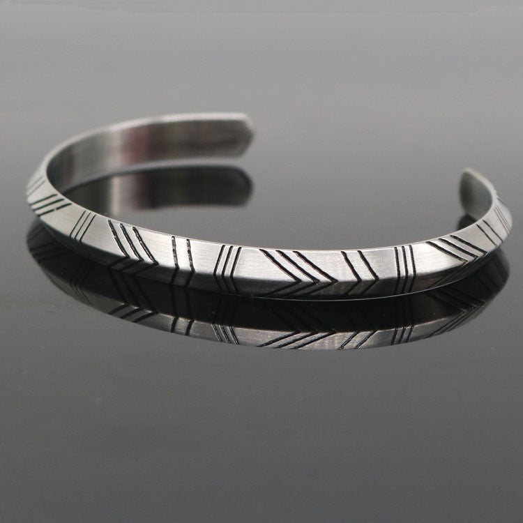Luxury Metal Bracelet with engraved diagonal lines on brushed silver surface resting on reflective black background