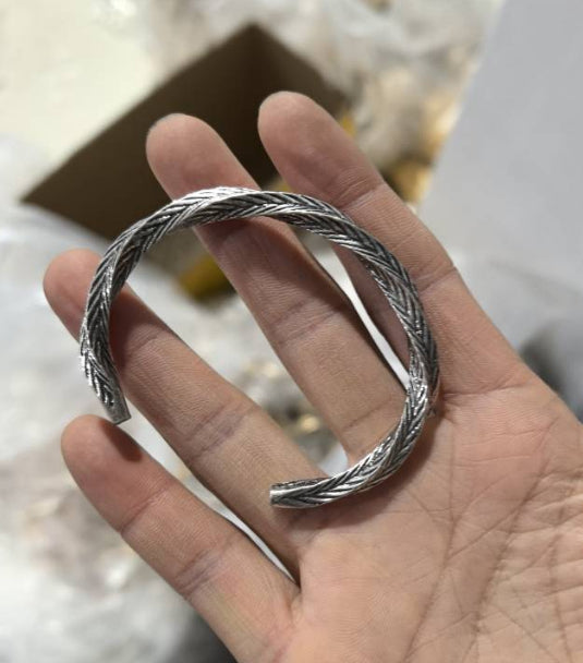 Hand holding a twisted open-ended silver Luxury Metal Bracelet with intricate braided detailing.